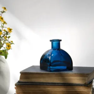 Blue glass vase on stacked antique books beside yellow flowers.