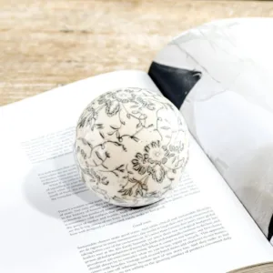 A decorative ball with floral patterns and a folded cloth on an open book.
