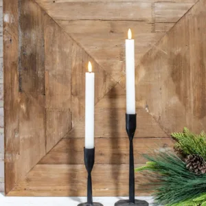 Two candles are lit on a table next to a wooden wall.