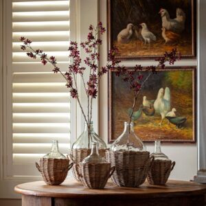 Decorative glass bottles with dried flowers on a wooden table beneath duck paintings.
