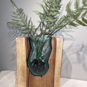 Green fern leaves in a green glass vase on a wooden stand.