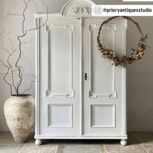 Elegant white vintage wardrobe with decorative wreath and large ceramic vase.