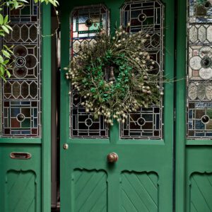 Green door adorned with a festive wreath and intricate glass panels.