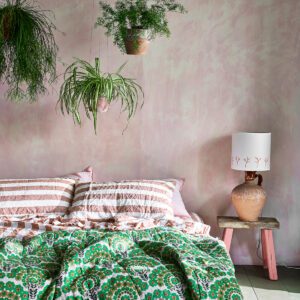 Cozy bed with green patterned bedding and hanging plants against a soft pink wall.