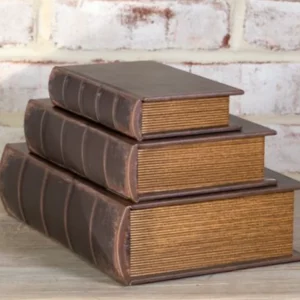 Three vintage brown books stacked against a white brick wall.