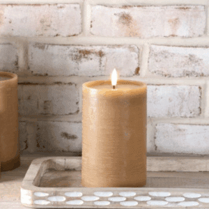 Lit beige candle on a tray against a white brick wall.
