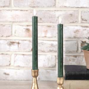 Two green taper candles in brass holders against a white brick wall.