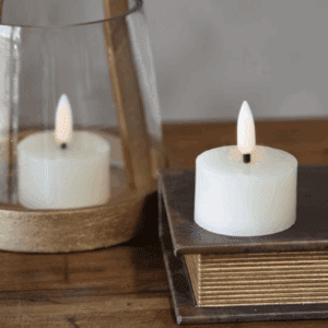 A lit white candle inside a glass holder and another on stacked books.